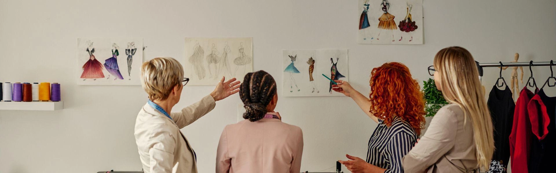 Designers da indústria da moda apontando para esboços pendurados na parede e conversando sobre planos de projeto.