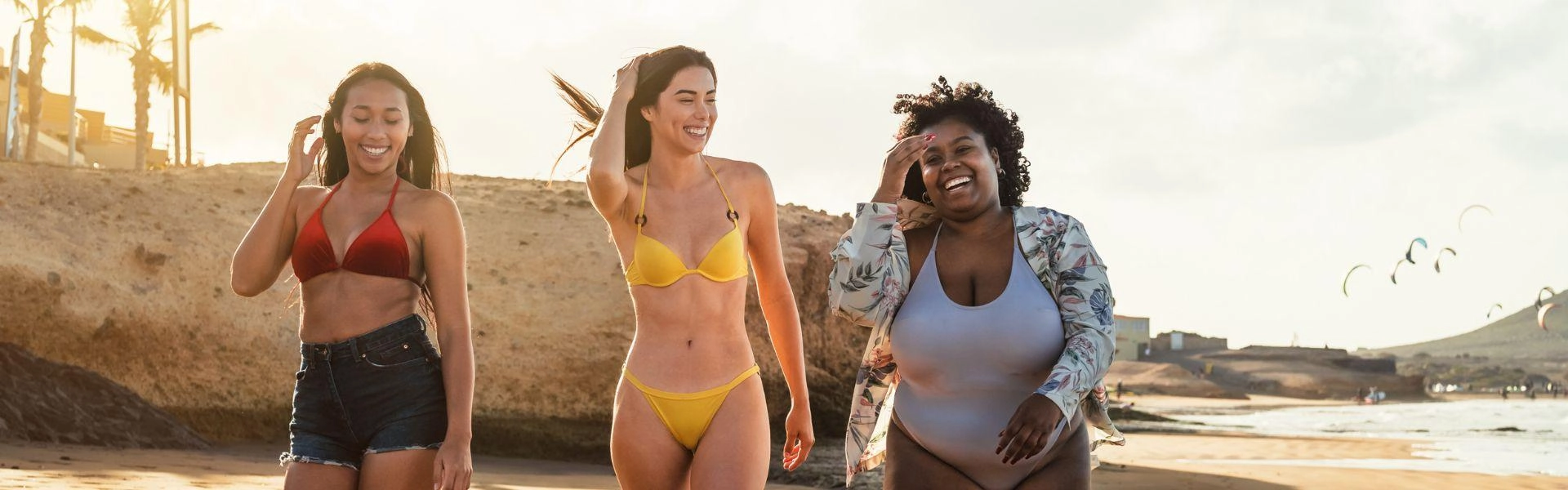 Três mulheres andando na praia com roupa de banho.
