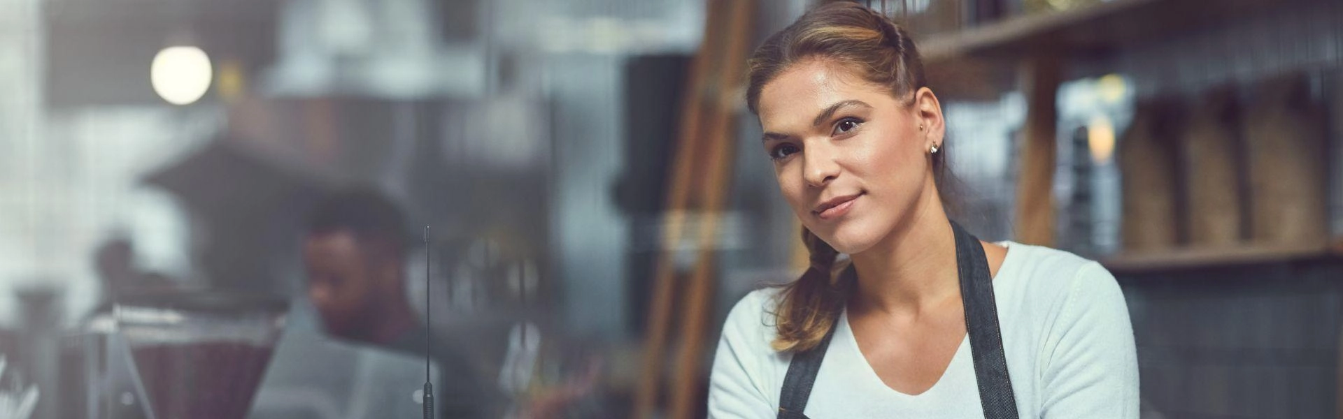 Mulher empreendedora, branca, de cabelos loiros e vestindo uma blusa branca com avental escuro.