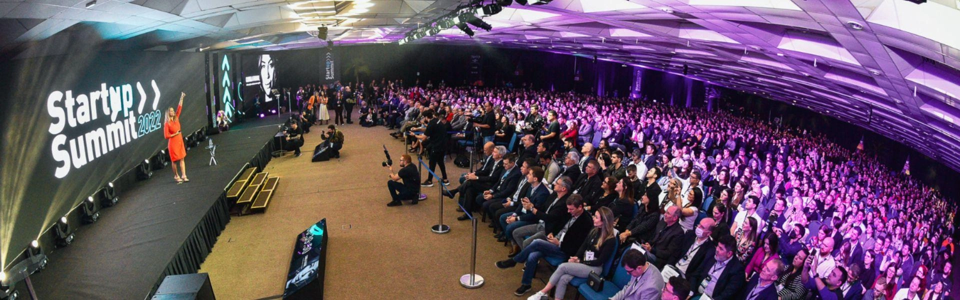 Palco de apresentação do Startup Summit e diversos participantes na plateia.