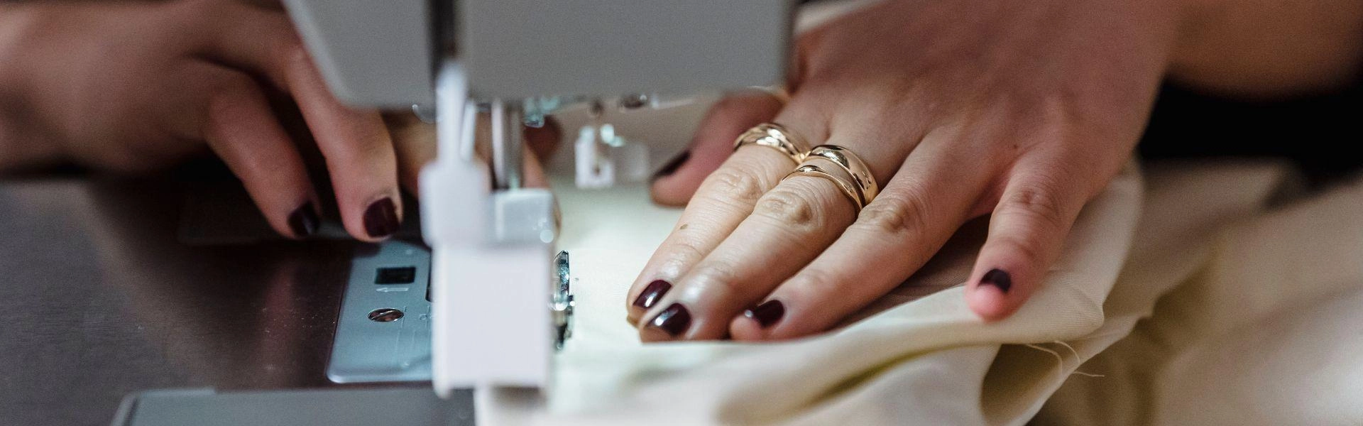 Mãos femininas produzindo uma peça de roupa com o auxílio de uma máquina de costura.