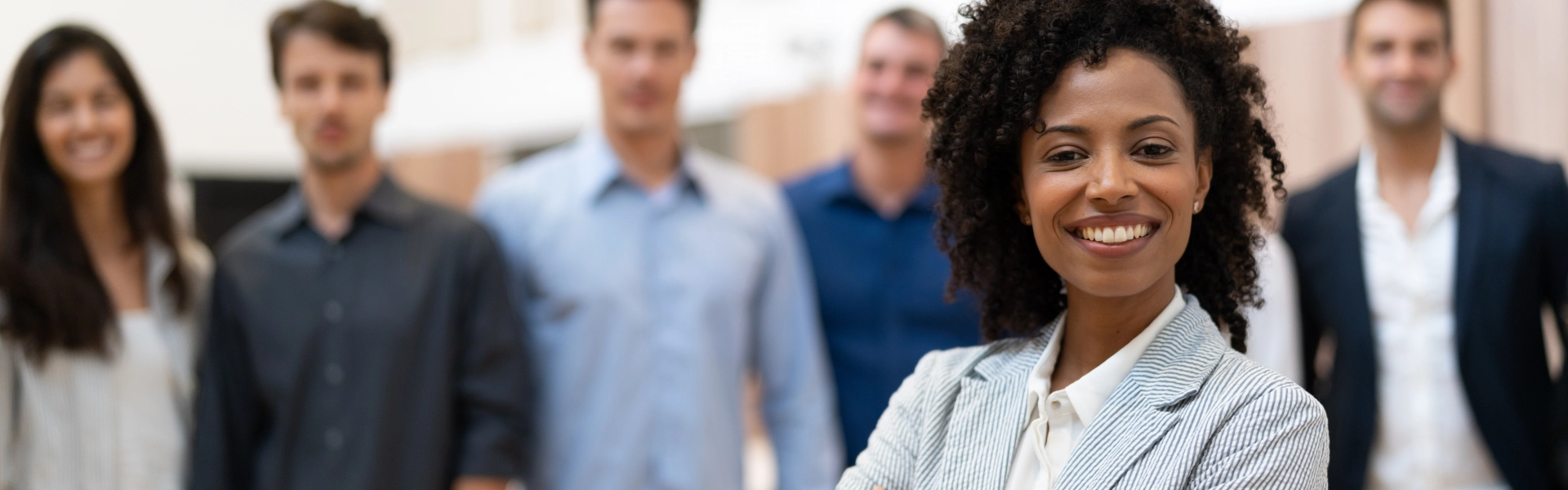 Mulher negra sorrindo com colegas de trabalho ao fundo.