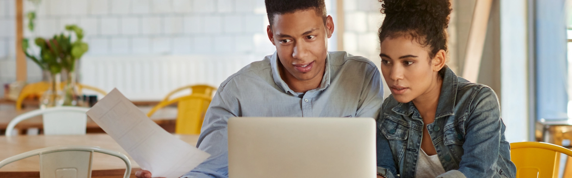 Homem negro e mulher negra fazem planejamento em notebook.