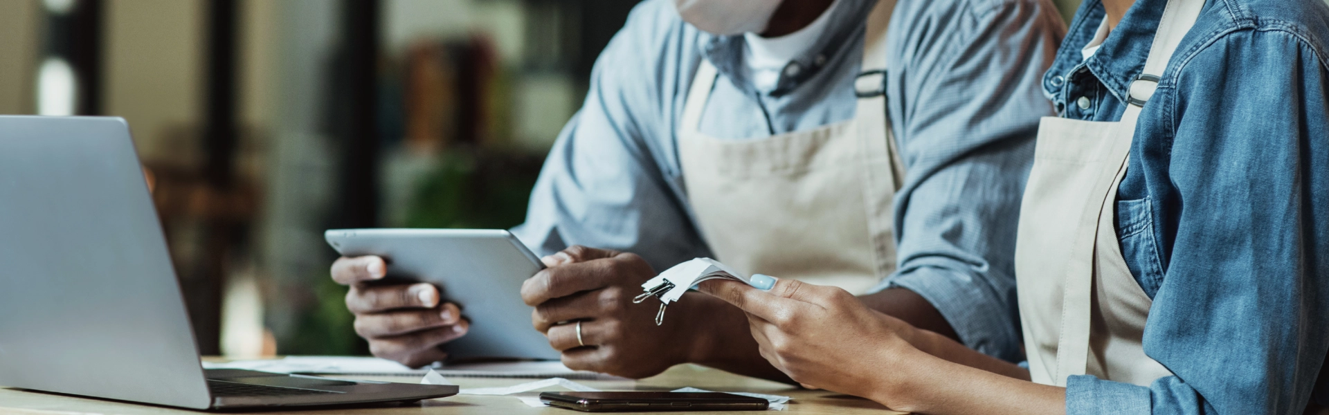 Homem e mulher negros conferem contas em tablet e notebook.