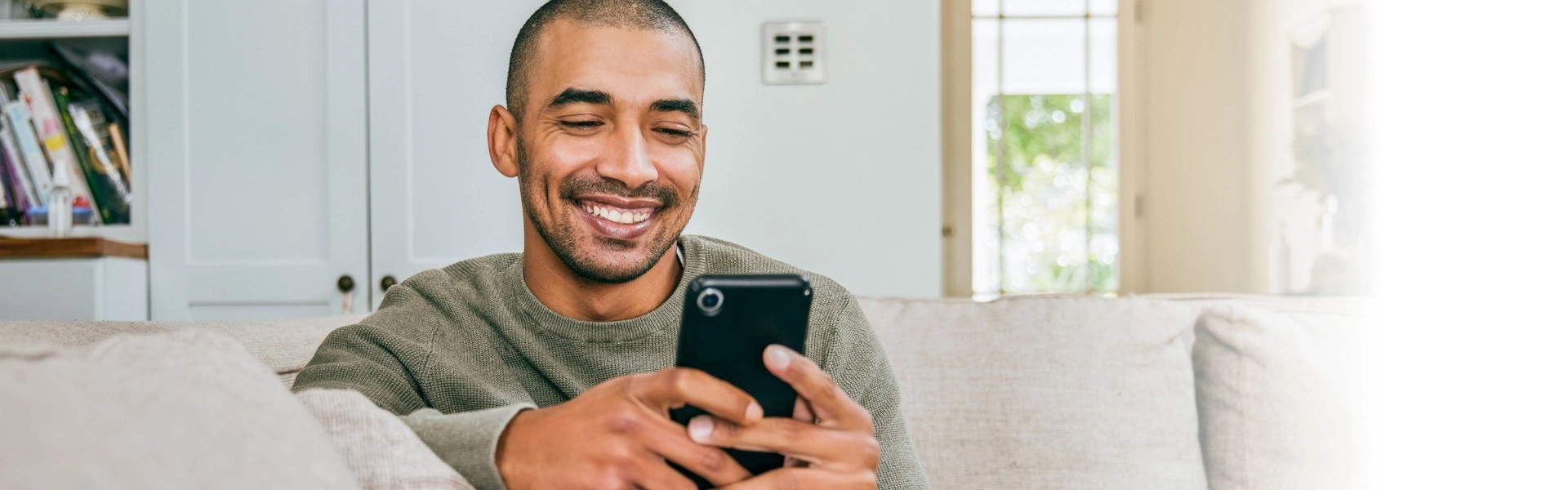 Homem negro sorrindo enquanto utiliza um smartphone.