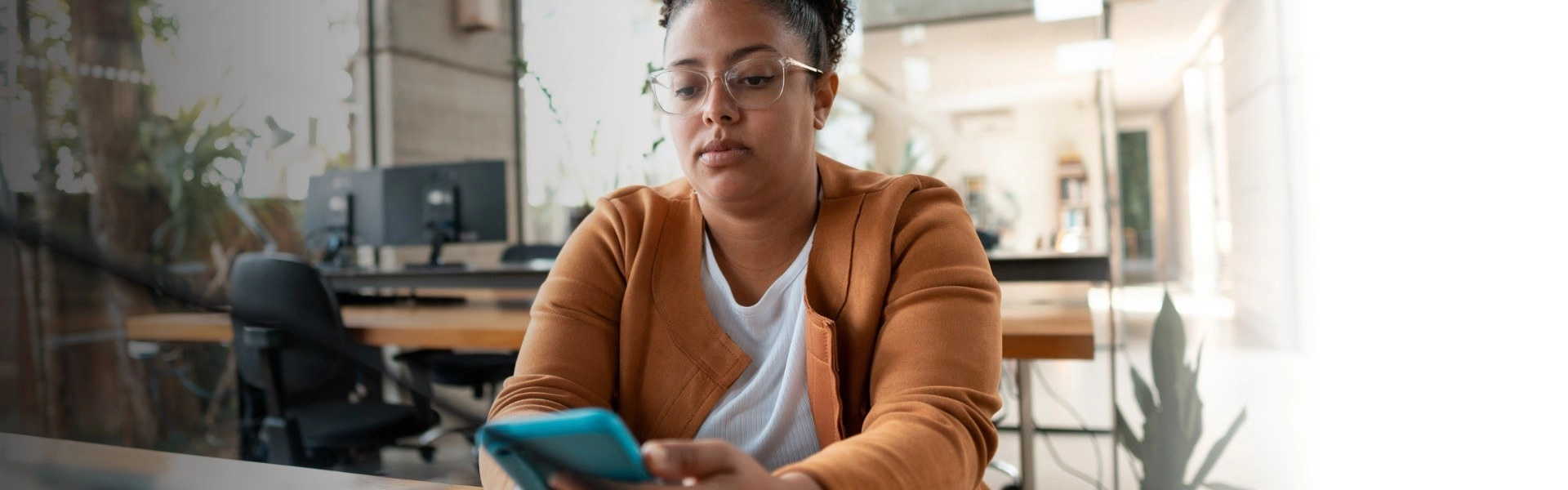Mulher negra com cabelos amarrados e óculos transparente pesquisa sobre funil de vendas em smartphone