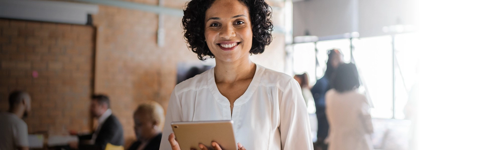 Mulher negra sorrindo com tablet prata na mão.