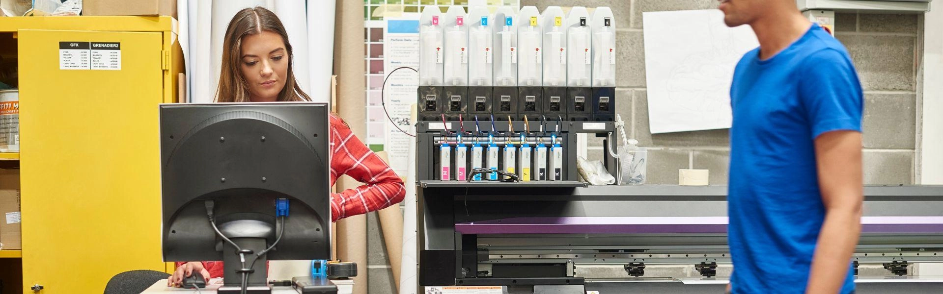 Mulher branca mexendo no computador enquanto trabalha em uma gráfica.