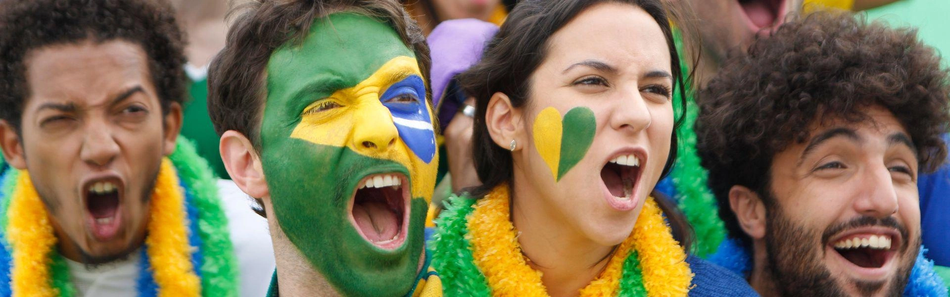 Torcedores de futebol brasileiro com a cara pintada com a bandeira do Brasil.