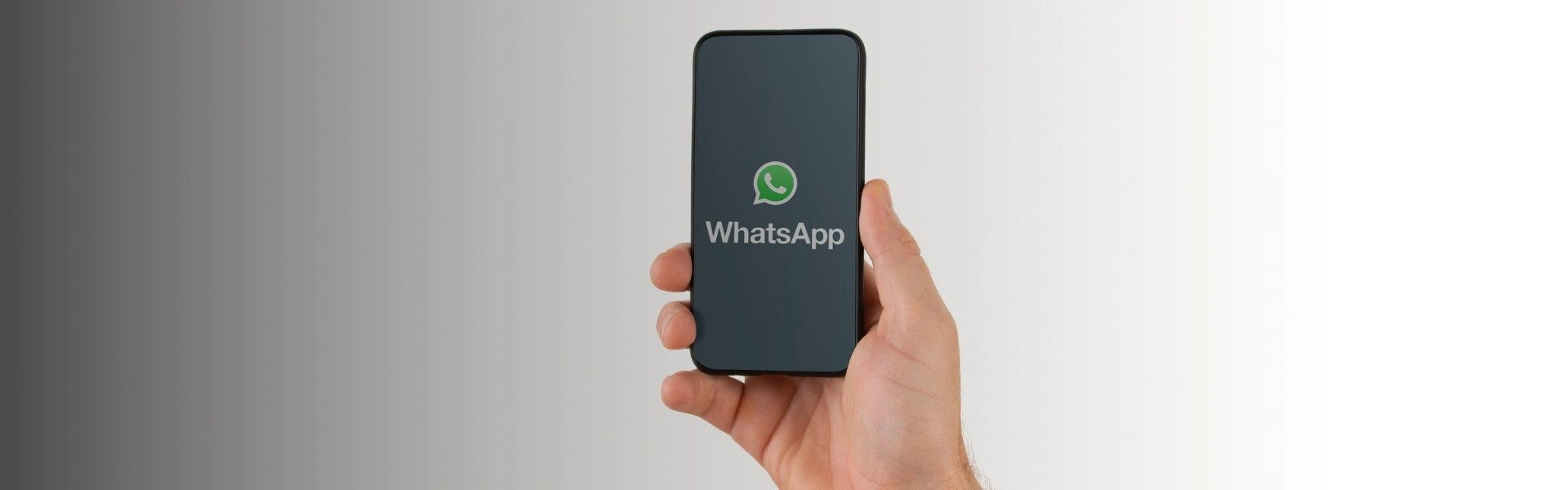 Mão masculina segurando um celular que exibe a logo do WhatsApp na tela