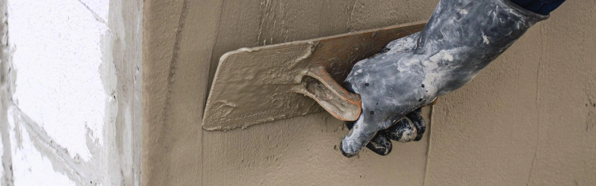 Trabalhador de obras segurando uma espátula de gesso enquanto passa na parede.