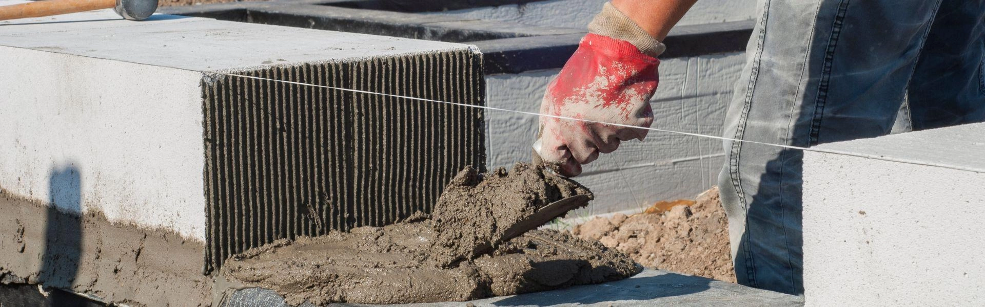 Aproximação da mão de um trabalhador mexendo com cimento e bloco de tijolo.