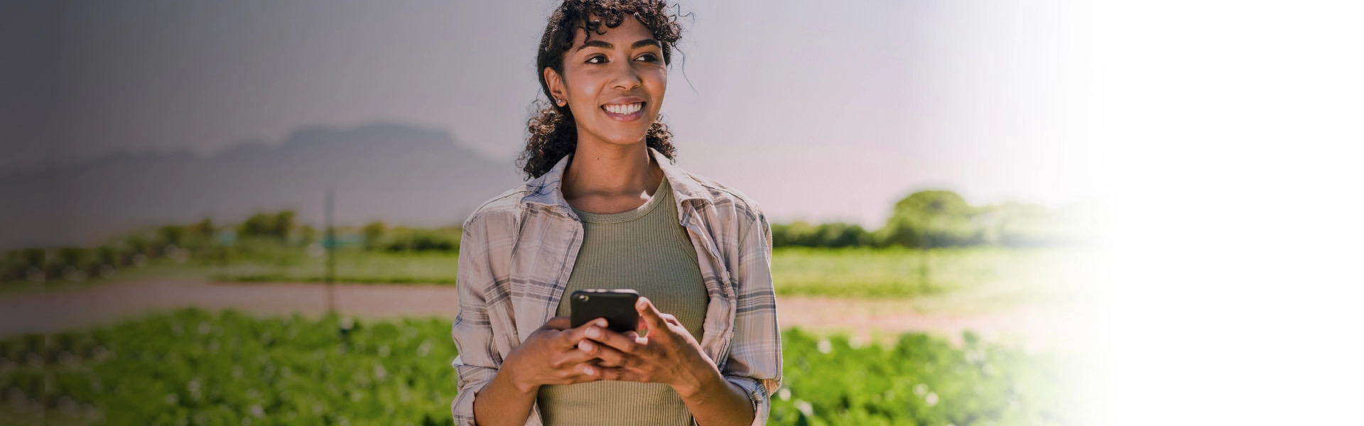 Mulher negra sorrindo segurando um celular.