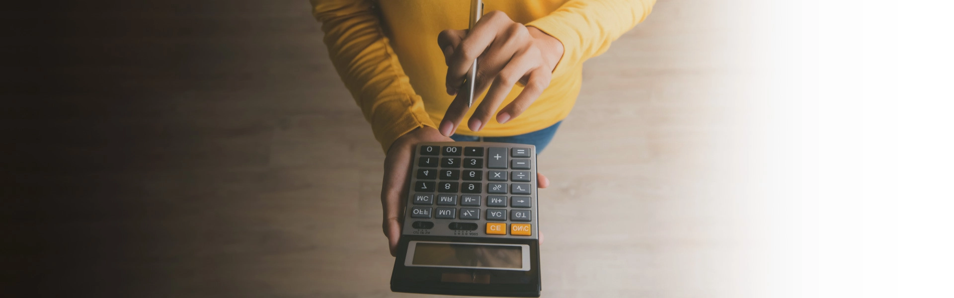 Mãos de uma mulher branca segurando uma calculadora e uma caneta.