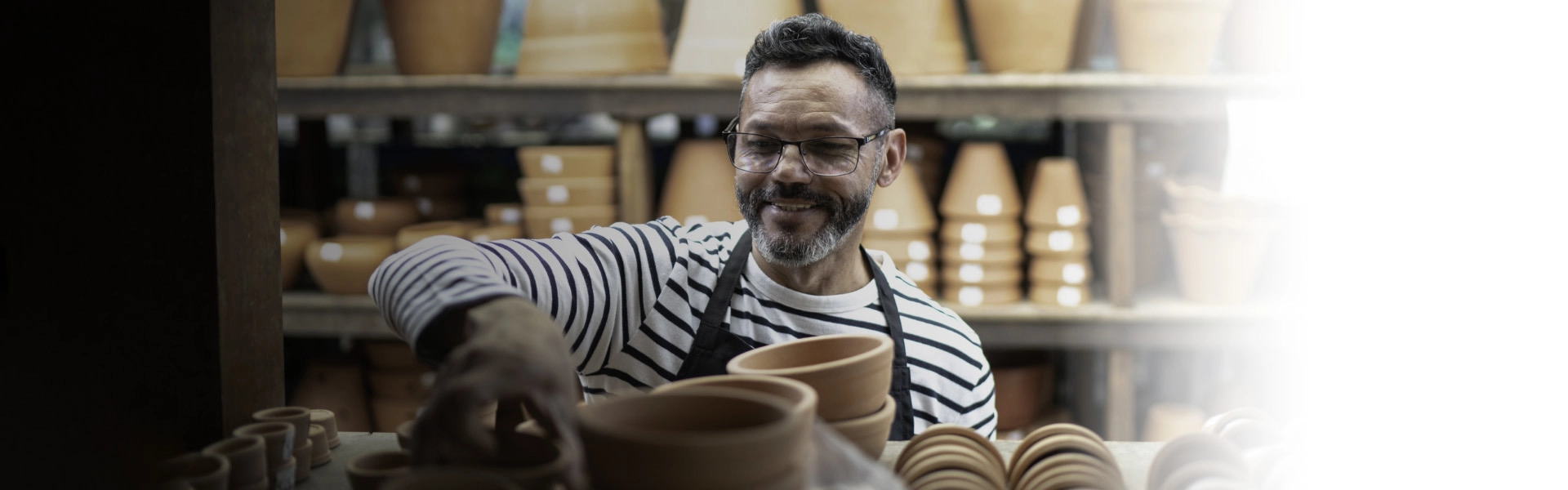 Homem branco sorrindo enquanto organiza peças feitas de barro.