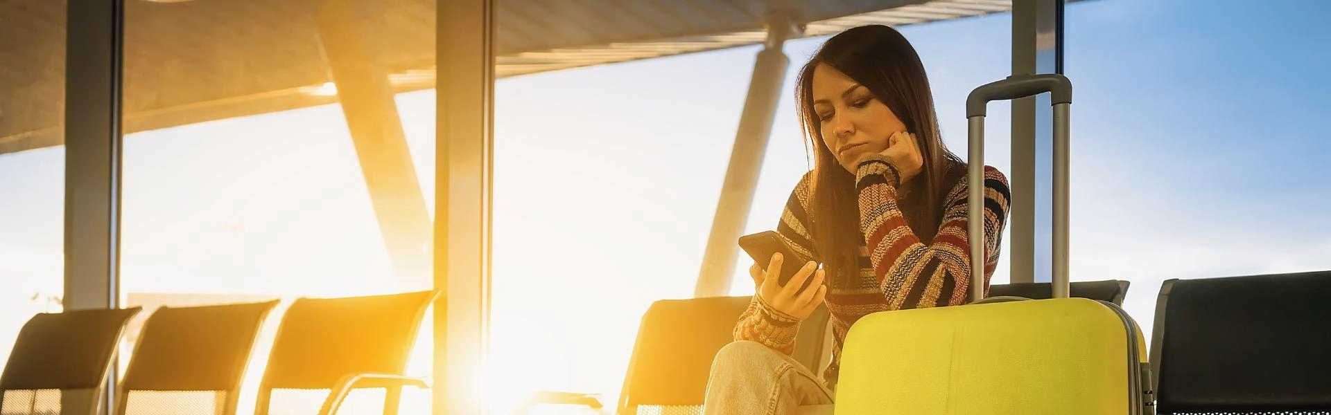 Mulher sentada em aeroporto mexendo no celular.