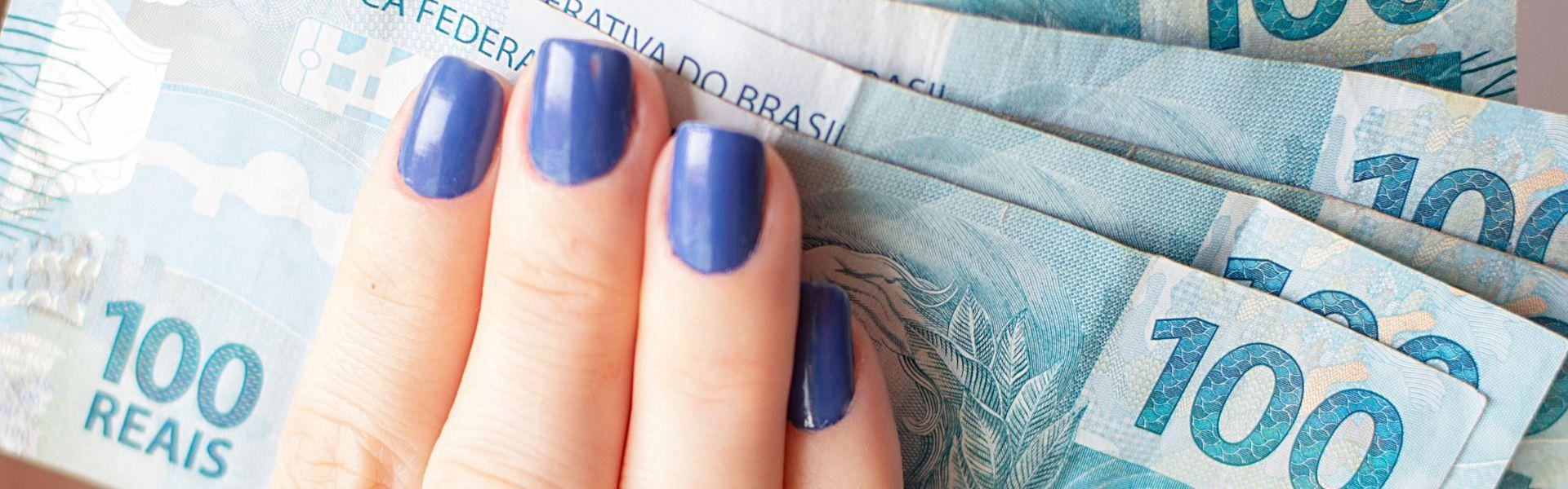 Uma mão feminina segurando várias notas de cem reais