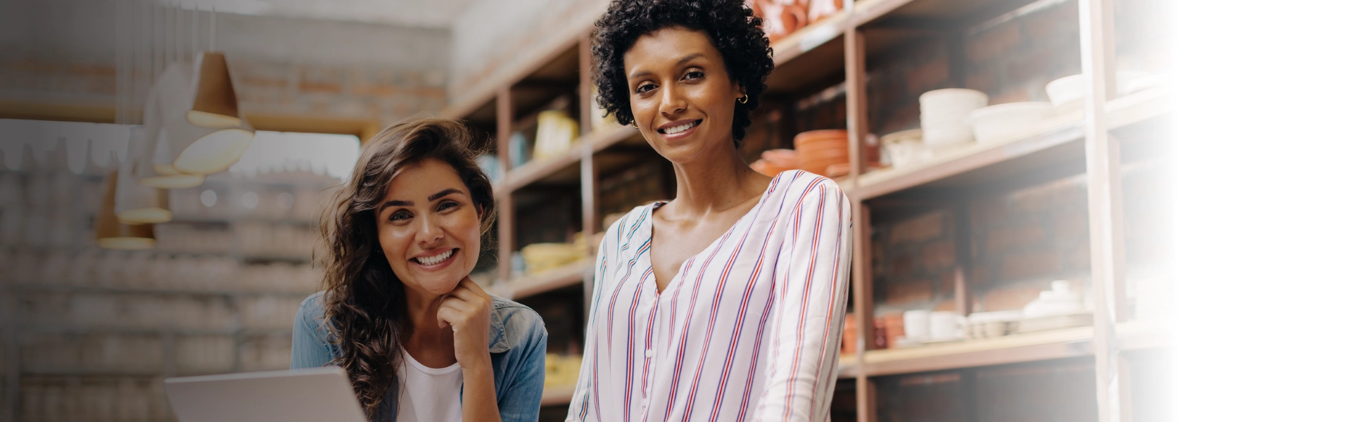 Duas mulheres apoiadas em um balcão de loja sorrindo de forma otimista.