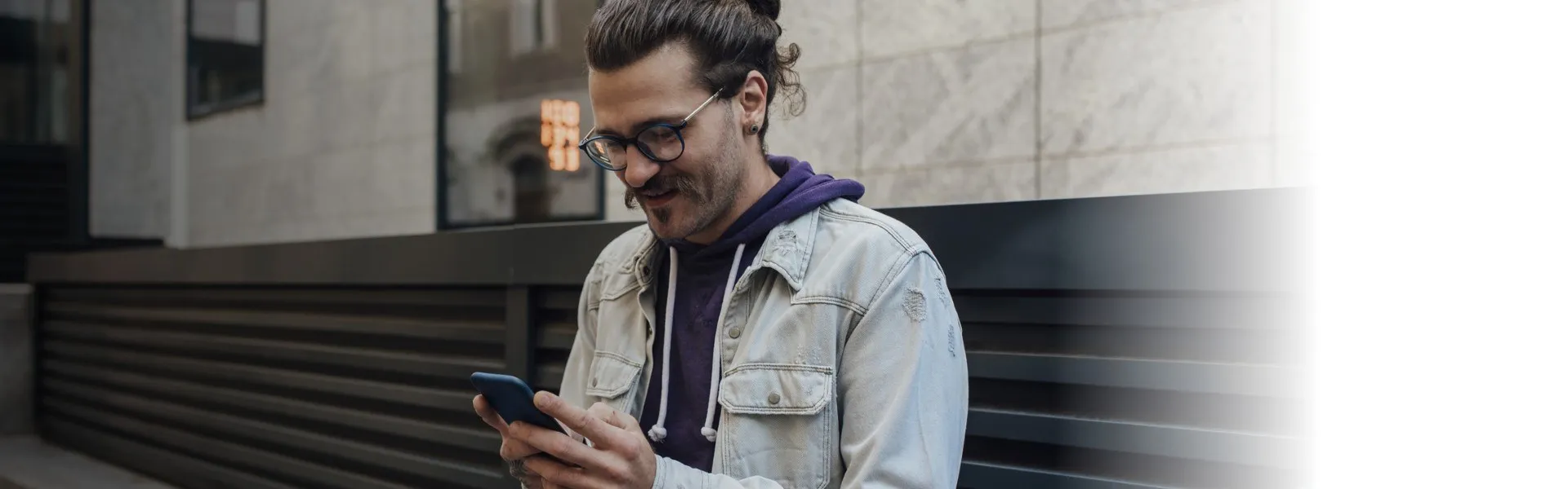 Homem branco sorrindo e enquanto olha a tela do celular.