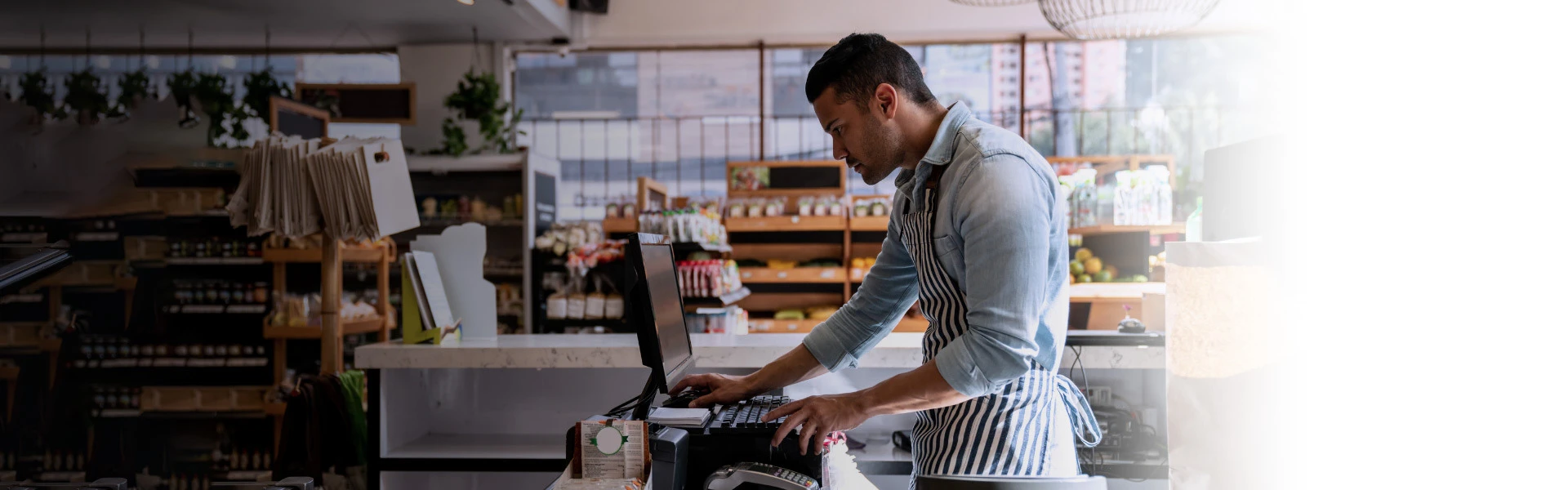 Homem branco usando um computador atrás do caixa de um mercado.