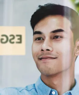 Homem feliz ao colar um post-it escrito ESG em uma parede de vidro.