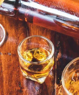 Uma mesa de madeira com uma garrafa de cachaça e três copos em cima.