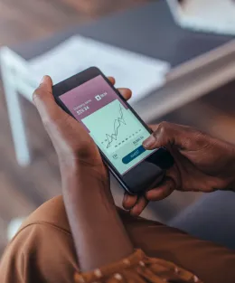 Celular nas mãos de uma pessoa com gráficos financeiros na tela.