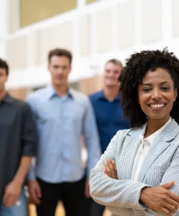 Mulher negra sorrindo com colegas de trabalho ao fundo.
