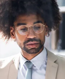 Homem negro vestindo óculos de grau e terno.