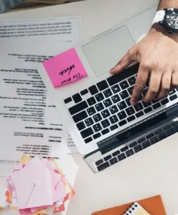 Uma reunião vista de cima com mãos utilizando notebook e post-its