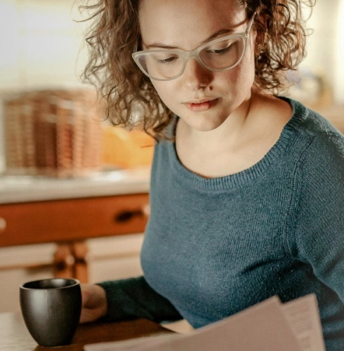 Mulher branca lendo papel com xícara na mão
