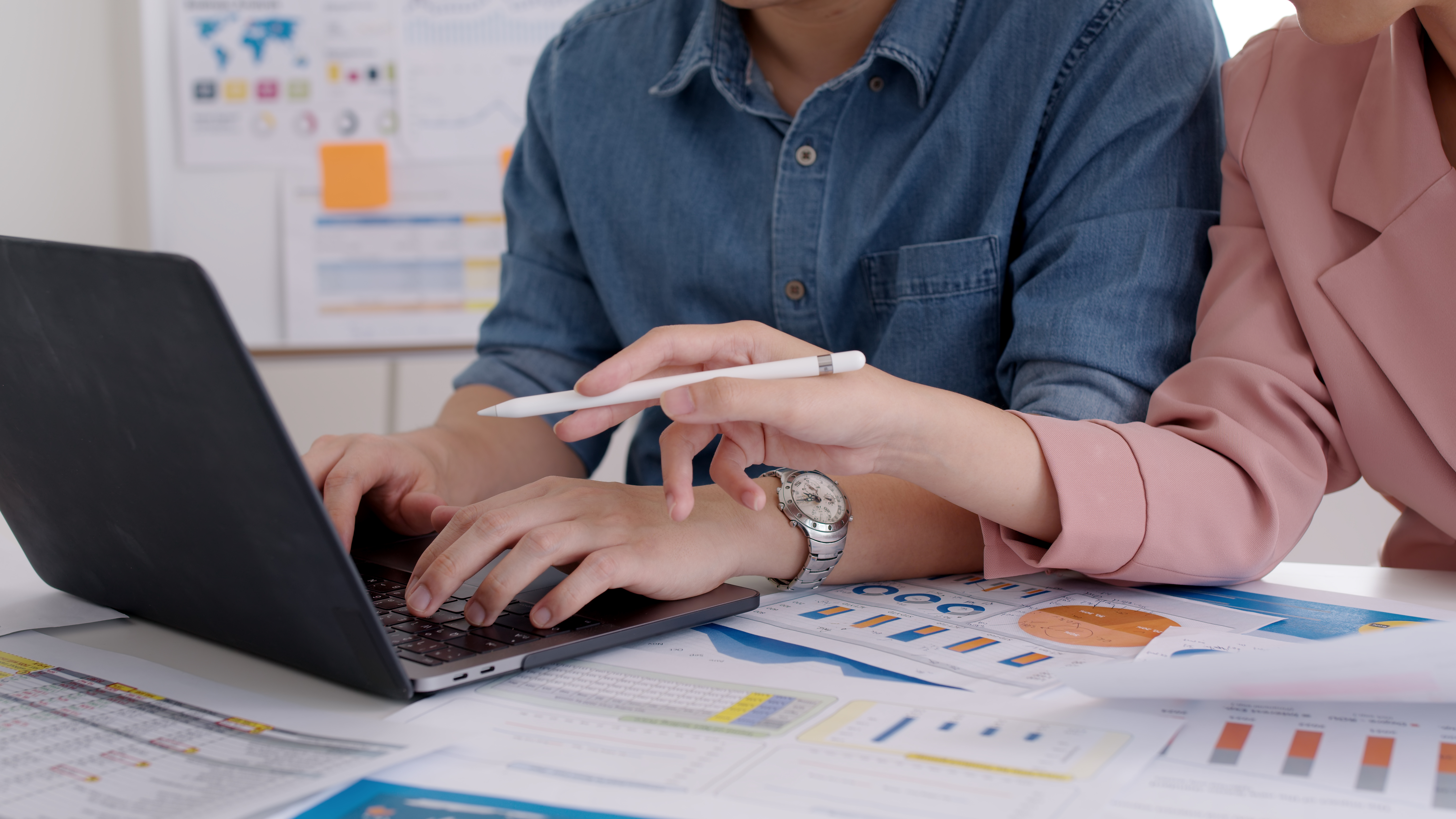 Duas pessoas colaborando em um projeto, analisando gráficos e dados em um computador portátil durante uma reunião de negócios.
