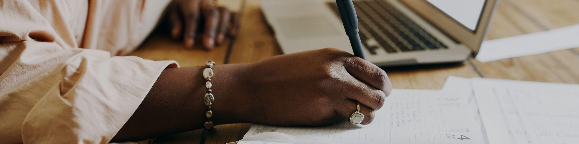 Empreendedora escrevendo anotações ao lado de notebook e planilhas, ilustrando planejamento financeiro e captação de recursos para negócios liderados por mulheres.
