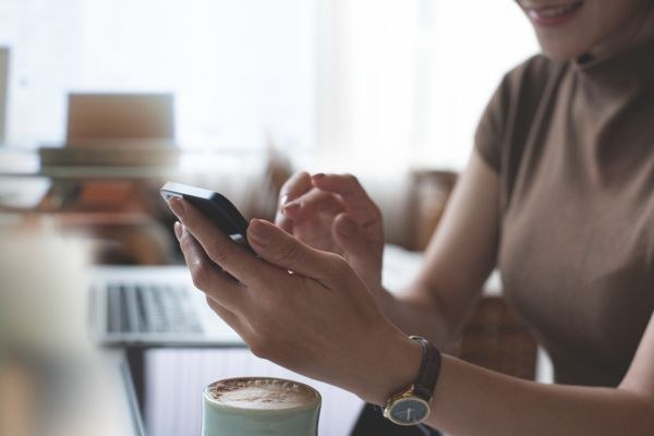 Mulher utilizando smartphone enquanto toma café, representando o uso da tecnologia e conexão com o mundo digital.