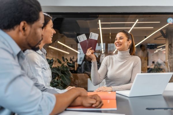 Mulher sorridente segurando passaportes em uma mesa de reunião, conversando com amigos sobre viagem e planejamento.