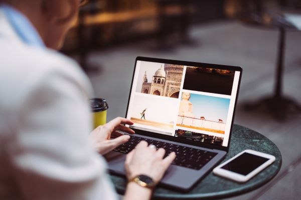 Pessoa trabalhando em um laptop em uma mesa de café, visualizando imagens de viagem e monumentos icônicos.