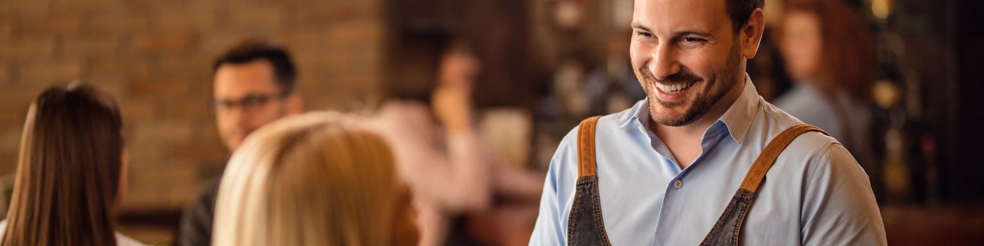 Homem sorridente atendendo clientes em um ambiente de bar ou restaurante, transmitindo acolhimento e cordialidade ao público.