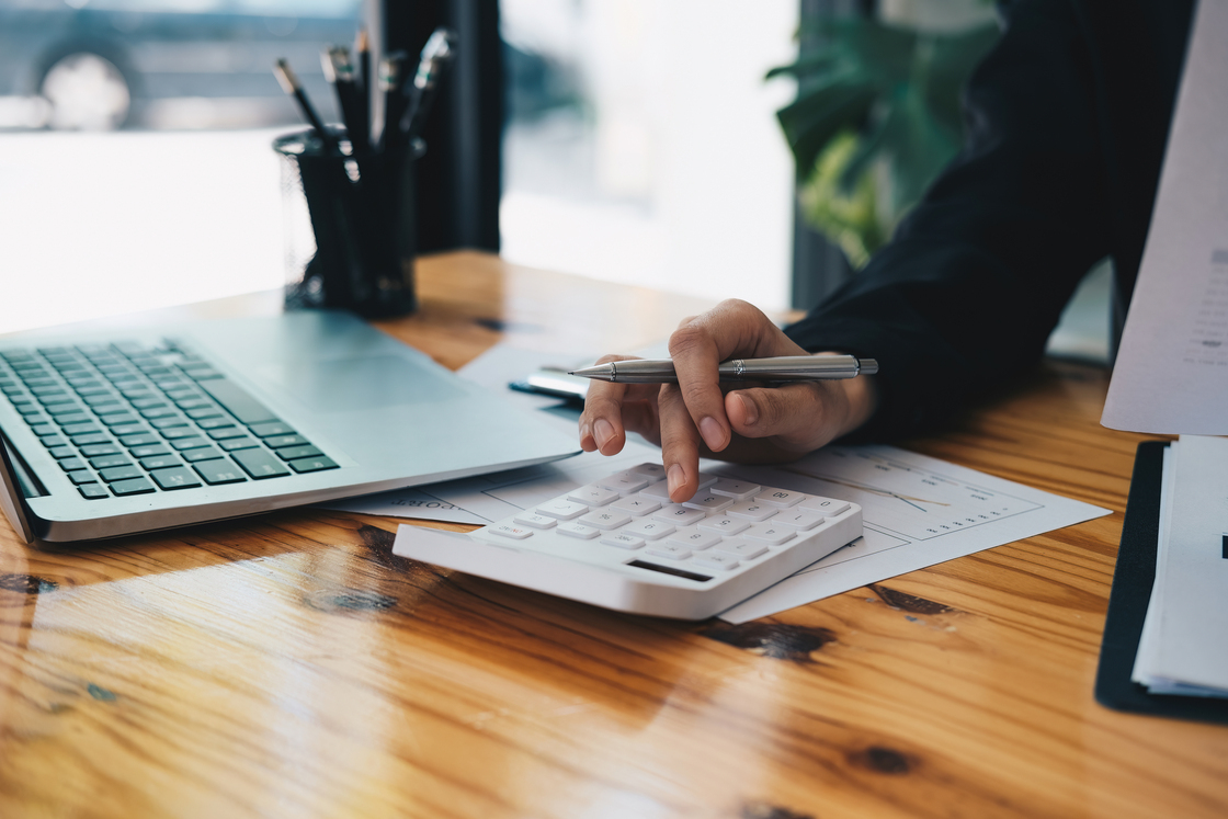 Pessoas trabalhando em escritório com um laptop, calculadora e documentos, focando em tarefas administrativas e financeiras.