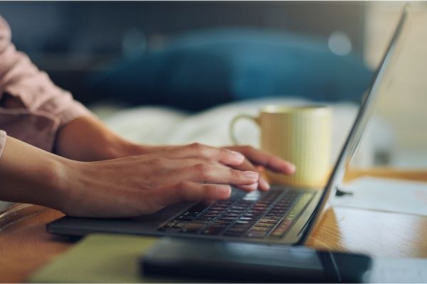 Pessoa digitando em um laptop sobre a mesa, com uma caneca ao lado, capturando um momento de trabalho remoto e produtivo.