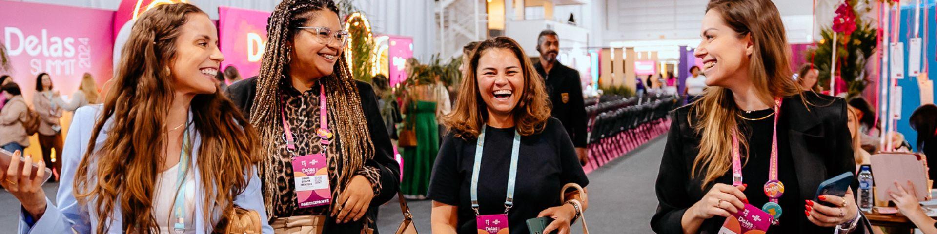 Mulheres participantes do Delas Summit caminhando e conversando animadamente durante o evento, simbolizando networking e troca de experiências entre empreendedoras.