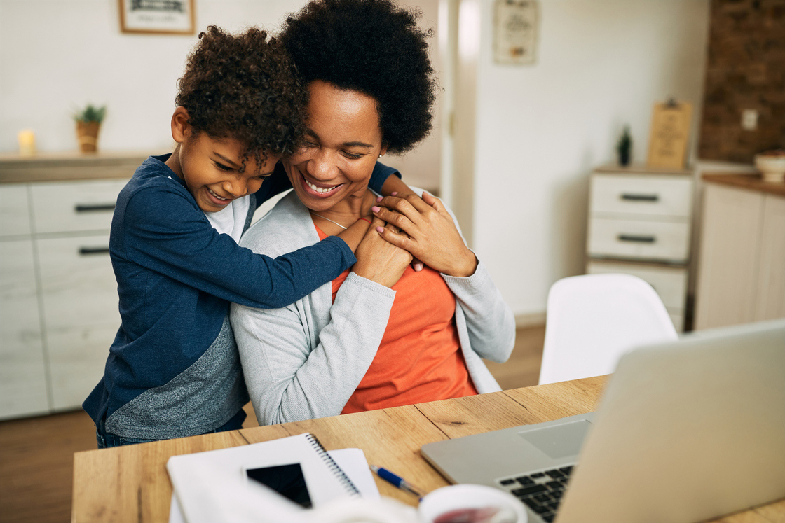 Imagem de uma mãe e um filho em um ambiente doméstico, mostrando afeto e alegria enquanto trabalham juntos em um computador. Essa imagem é perfeita para ilustrar momentos de carinho e conexão familiar, ideal para conteúdos sobre maternidade e relações familiares.