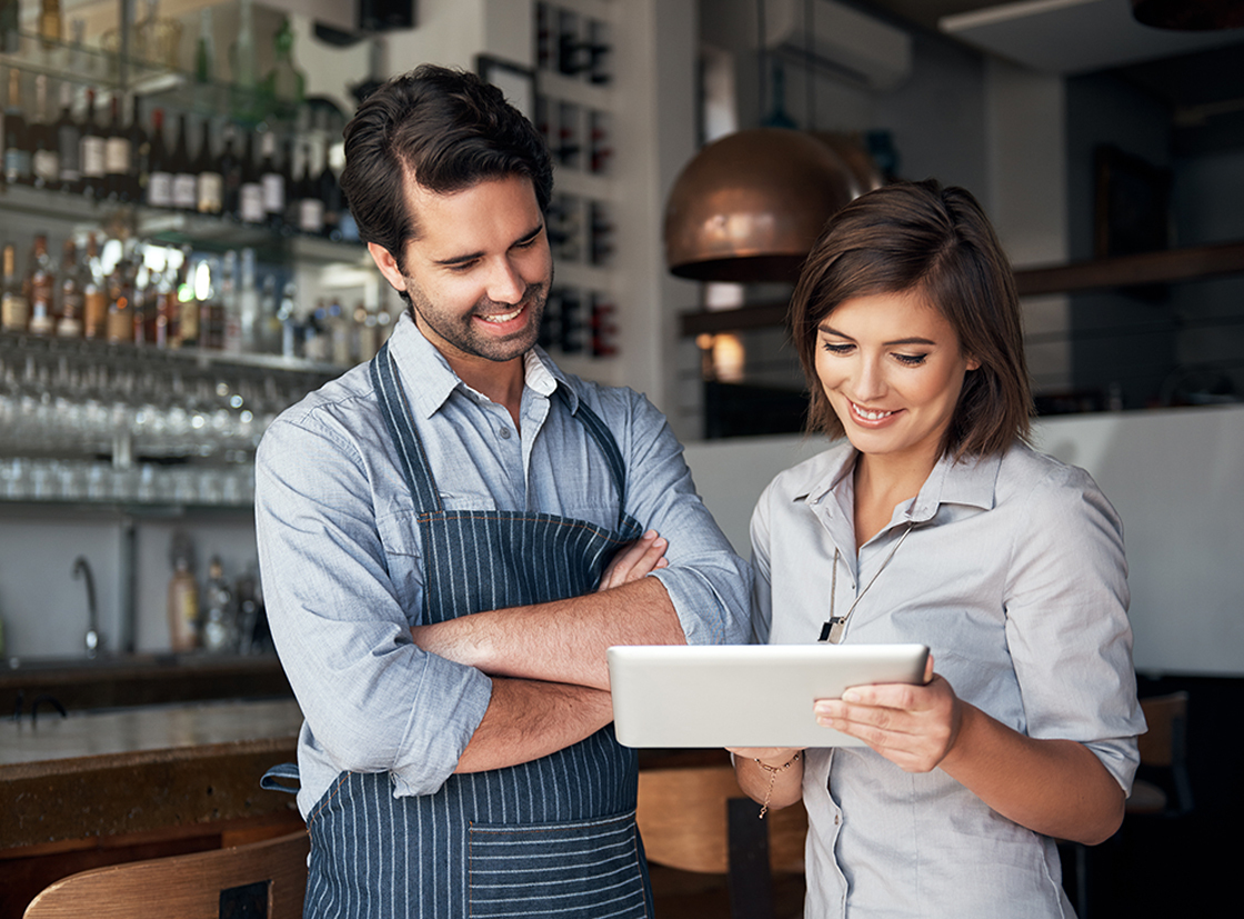 Profissionais de restaurante analisam informações em tablet, mostrando interação e trabalho em equipe no ambiente de cozinha.