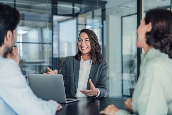 Reunião de negócios com mulher sorridente apresentando ideias em escritório moderno. Visão de três profissionais colaborando e compartilhando experiências.