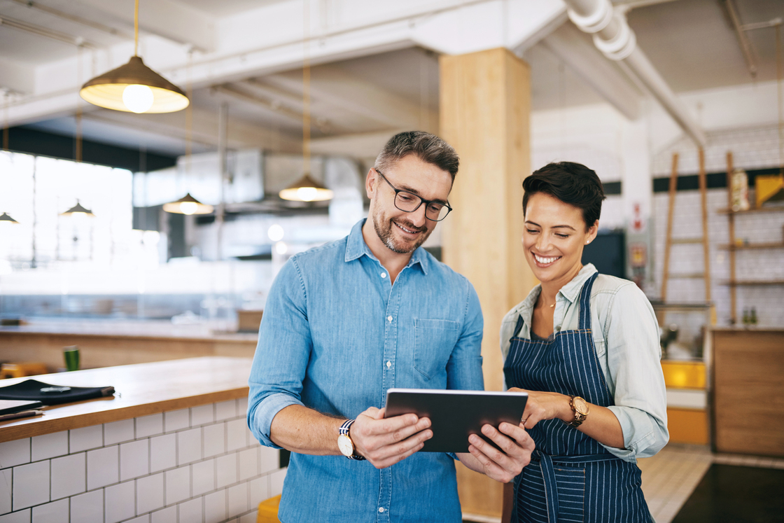 Dois profissionais conversando e analisando informações em um tablet em um ambiente de restaurante moderno e iluminado.