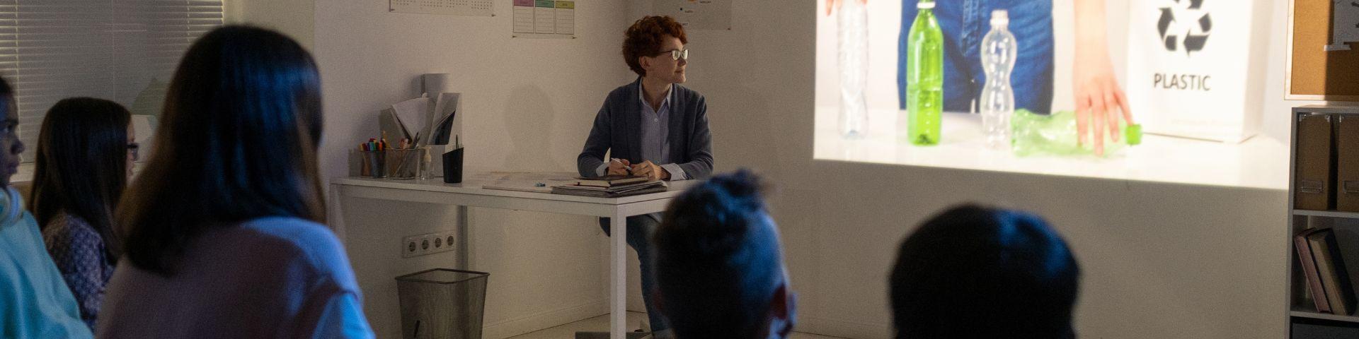 Alunos participando de um filme sobre reciclagem com foco em plástico, em ambiente de sala de aula moderna, com tela de projeção.