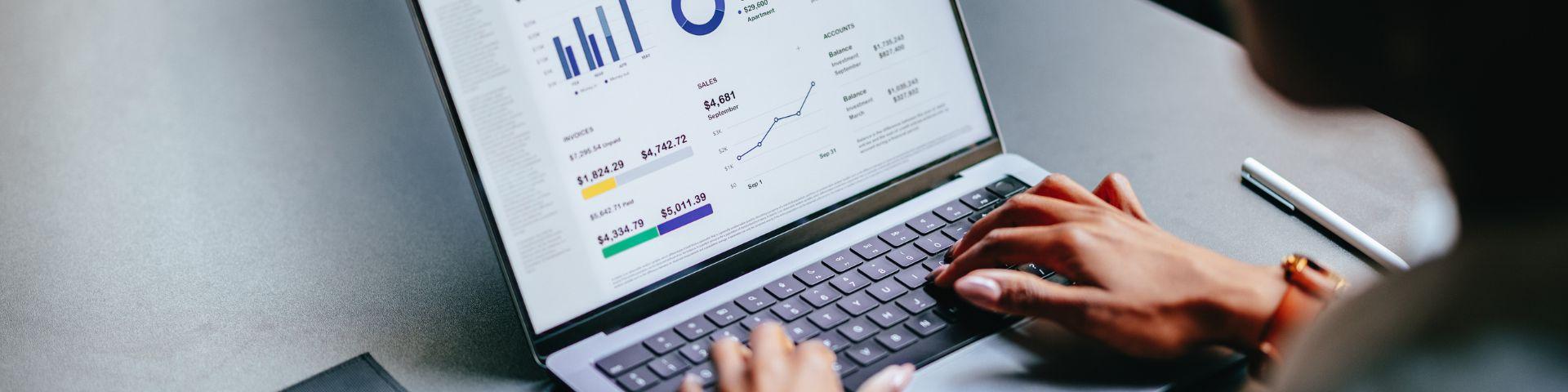 Pessoa analisando gráficos de desempenho financeiro em um laptop, com foco em crescimento de investimentos e análise de mercado.