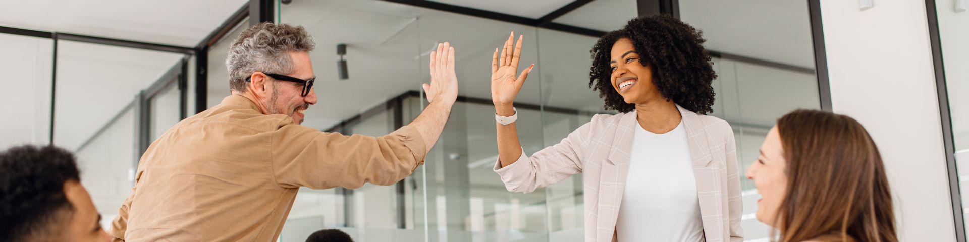 Profissionais comemorando com um high five em ambiente corporativo, simbolizando engajamento, colaboração e sucesso na adoção da inovação organizacional.