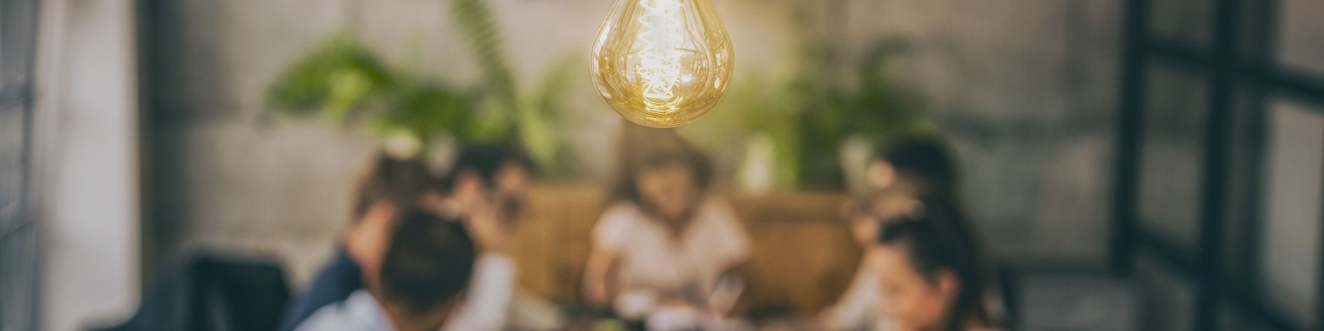 Imagem de um ambiente corporativo com pessoas conversando ao redor de uma mesa, iluminação aconchegante e ambiente moderno.