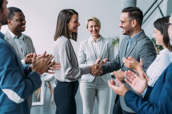 Grupo de profissionais celebrando um acordo com sorrisos e cumprimentos, mostrando a importância de boas parcerias de negócios.
