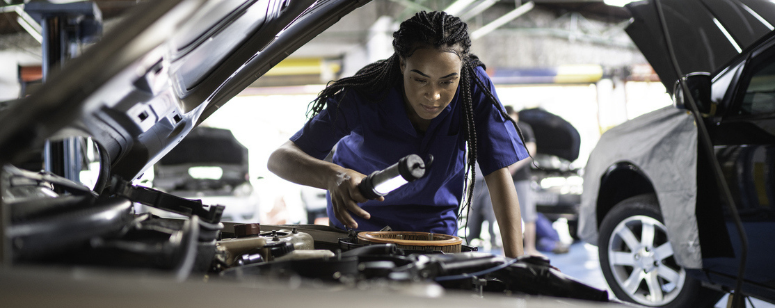 Mulher mecânica trabalhando em um carro, verificando o motor com ferramentas em uma oficina, foco em manutenção automotiva eficiente.